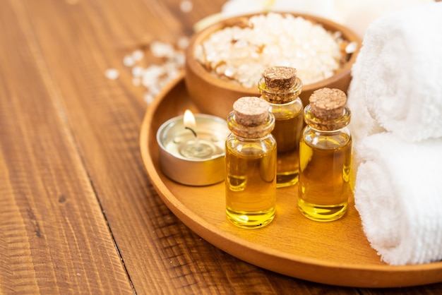 Free photo of sea salt, towel, essential oil in bottle and flowers on a classic wooden background.